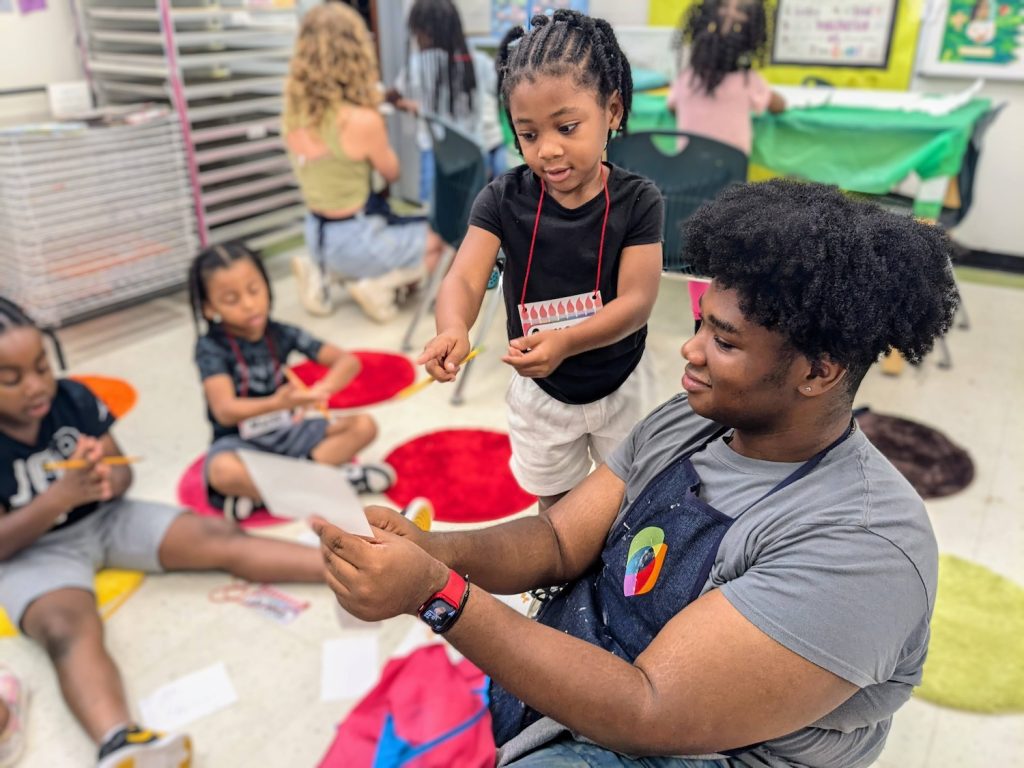 A kindergarten student explains a picture he drew to AFJ's summer intern, Justin.